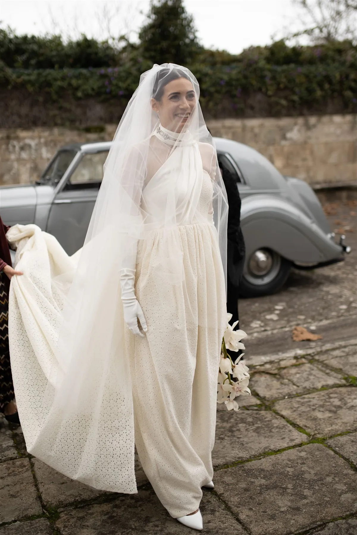 Cristina con velo largo, guantes y vestido vintage de Isabel Núñez junto a un coche clásico