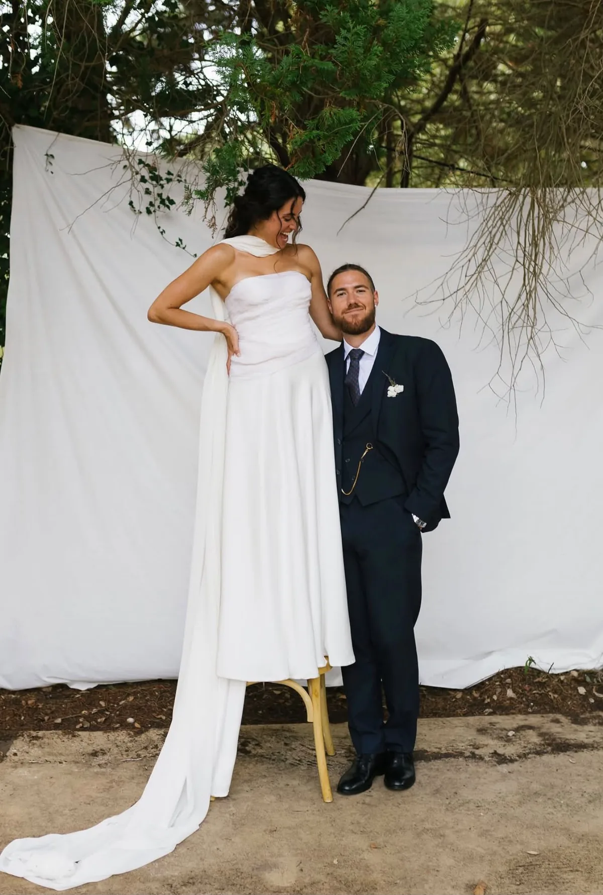 Sabela Abreu con vestido palabra de honor junto a su marido ante un telón blanco